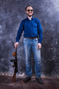 Makineli tüfekli, güneş gözlüklü, olgun bir adam.