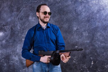 Makineli tüfekli, güneş gözlüklü, olgun bir adam.