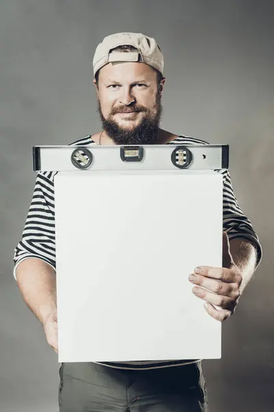 Joyful bearded craftsman with level and blanc cube studio portrait — Stock Photo, Image