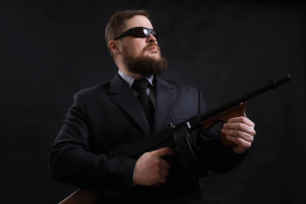 Ώριμος γενειοφόρος άνδρας με γυαλιά ηλίου ντυμένος με κοστούμι με το όπλο Tommy — Φωτογραφία Αρχείου
