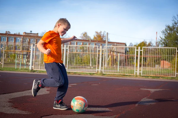 Rapaz bonito chutando a bola no parque infantil da cidade. — Fotografia de Stock