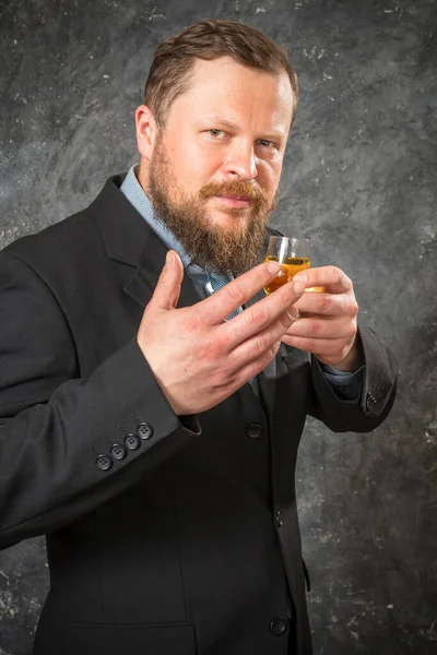Fast skäggig man i kostym provsmakning whisky i ett glas — Stockfoto