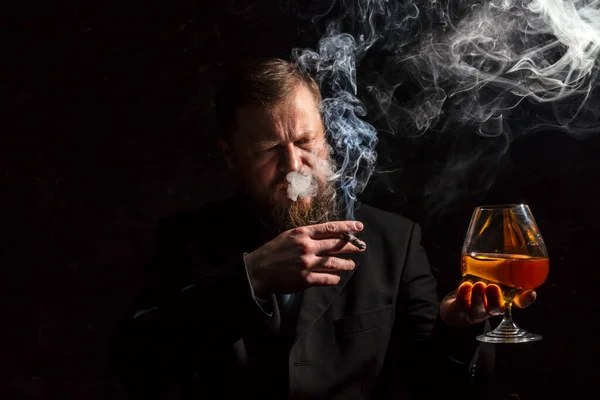 Solide homme barbu confiant en costume avec verre de whisky et cigare avec fumée — Photo