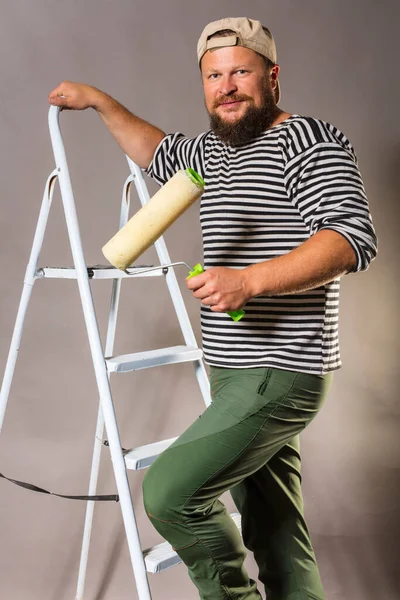 Vreugdevolle bebaarde ambachtsman met kwastroller en ladder — Stockfoto