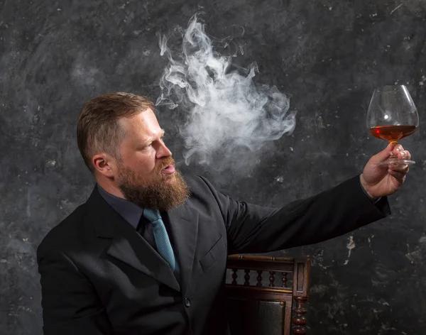 Solide homme barbu confiant en costume avec verre de whisky et de fumée — Photo