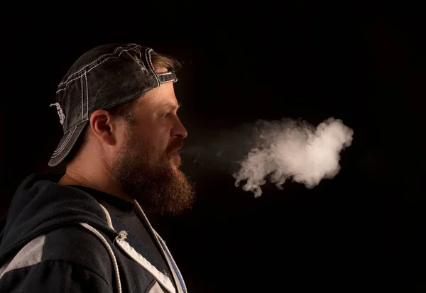 Hombre barbudo con gorra y ropa casual exhalando vapor de su boca — Foto de Stock