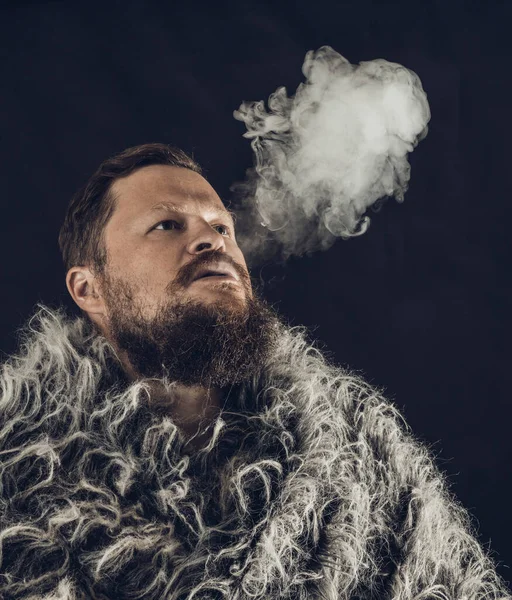 Solid bearded man dressed in a fur mantle exhaling vapour