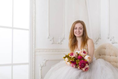 Çiçekleri olan, geniş etekli beyaz elbiseli güzel bir kadın kanepede oturuyor.