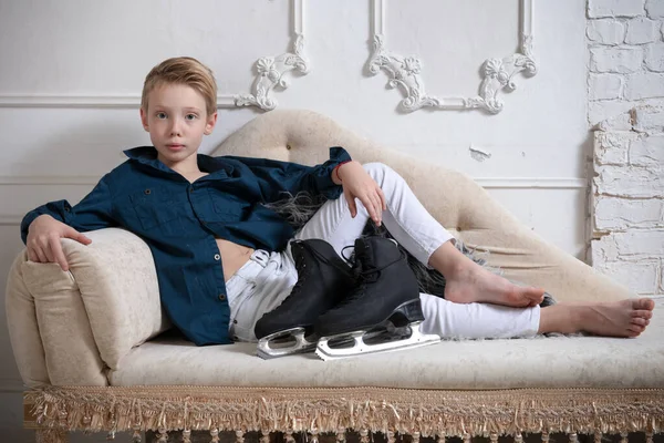 Joven patinador artístico vestido con jeans blancos y camisa azul relajándose en el sofá —  Fotos de Stock