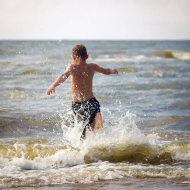 Genç neşeli çocuk deniz dalgalarında eğleniyor..