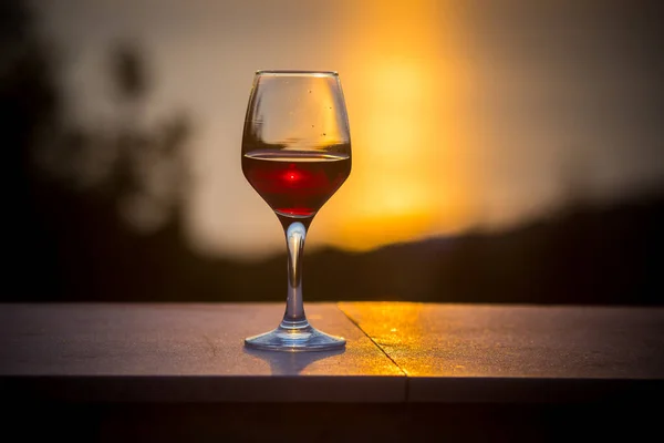 Сцена с бокалом вина, стоящим в одиночестве на естественном закатном небе — стоковое фото