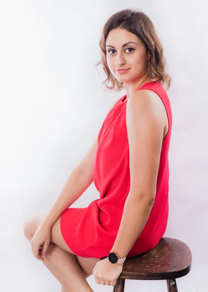 Piękna młoda pozytywna kobieta w czerwonej sukience siedzi na wysokim krześle — Zdjęcie stockowe