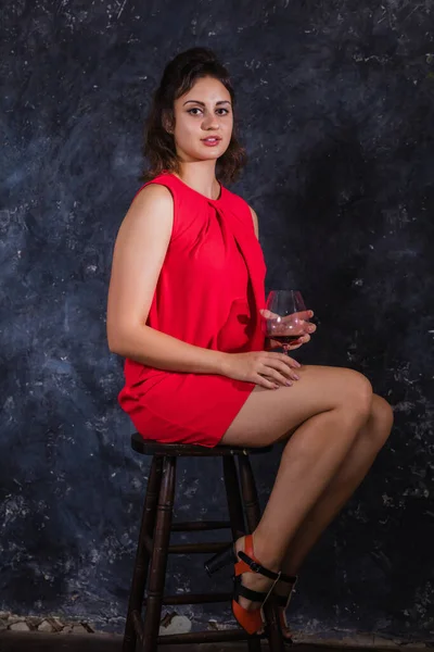 Piękna młoda dama w czerwonej sukience siedzi ze szklanką wina — Zdjęcie stockowe