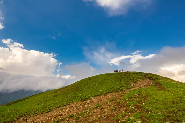 Красивый горный пейзаж в горах Кавказа с облаками, голубым небом и линией всадников далеко — стоковое фото