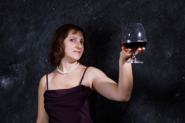 40 yaşında neşeli bir kadın, klasik giyinmiş, elinde şarap kadehi olan.