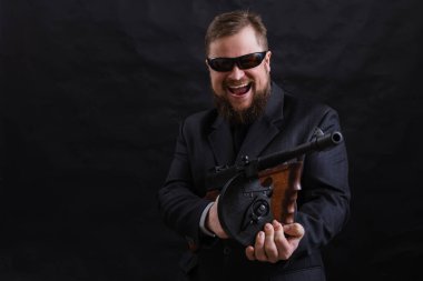 Tabancalı, takım elbiseli, güneş gözlüklü, olgun sakallı adam.