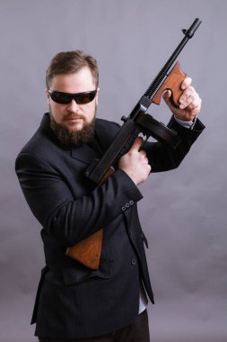 Güneş gözlüklü, takım elbiseli, Tommy Gun 'lı olgun bir adam.