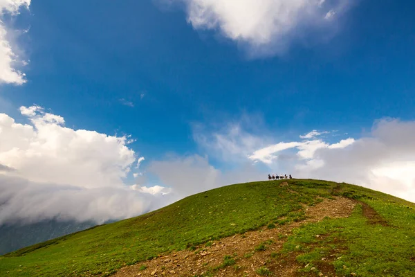 구름과 푸른 하늘 그리고 멀리서 말을 타고 달리는 사람들이 줄지어 있는 코카서스 산맥의 아름다운 산맥 — 스톡 사진