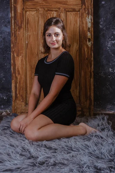 Piękna młoda kobieta w czarnej sukience siedzi na skórze futra przed zabytkowymi drzwiami — Zdjęcie stockowe