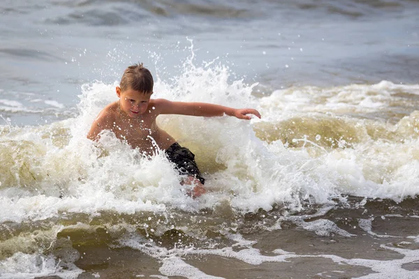 Młody wesoły chłopiec bawiący się na falach morskich. — Zdjęcie stockowe