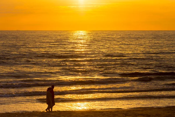 Люди прогуливаются по песчаному пляжу на закате — стоковое фото