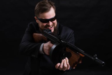 Tabancalı, takım elbiseli, güneş gözlüklü, olgun sakallı adam.