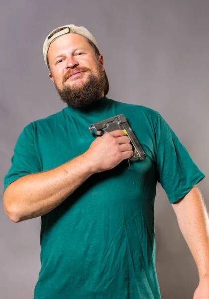 Artesano barbudo alegre en camiseta verde que se divierte con pistola de grapas —  Fotos de Stock