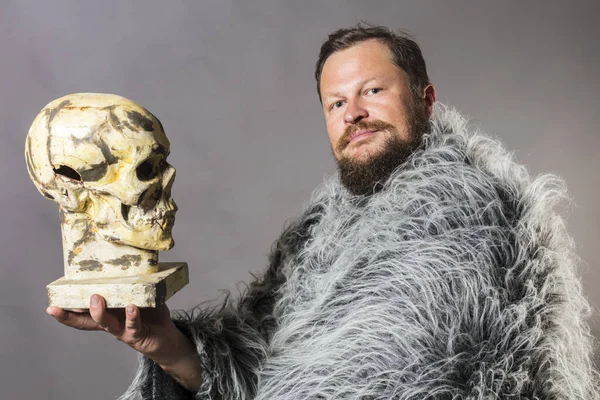 Solid bearded man in a fur mantle with skull studio portrait