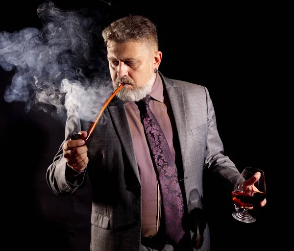 Solider bärtiger Mann im Anzug mit Glas Whisky rauchende Pfeife — Stockfoto