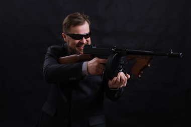 Tabancalı, takım elbiseli, güneş gözlüklü, olgun sakallı adam.