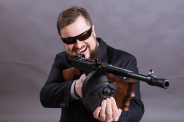 Güneş gözlüklü, takım elbiseli, Tommy Gun 'lı olgun bir adam.