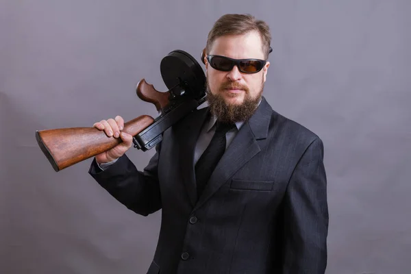 Dojrzały mężczyzna w okularach przeciwsłonecznych ubrany w garnitur z pistoletem Tommy — Zdjęcie stockowe