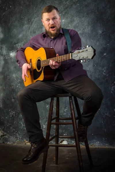 Mature musician plays acoustic guitar emotional studio portrait. — Stock Photo, Image