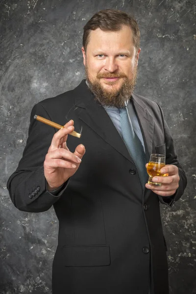 Fast säker skäggig man i kostym med glas whisky och cigarr — Stockfoto