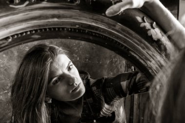 Genç, uzun saçlı, güzel kadın klasik aynanın önünde oturuyor.