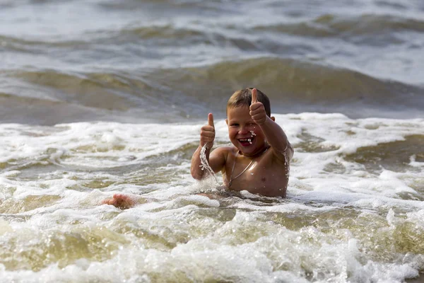 Młody wesoły chłopiec bawiący się na falach morskich. — Zdjęcie stockowe