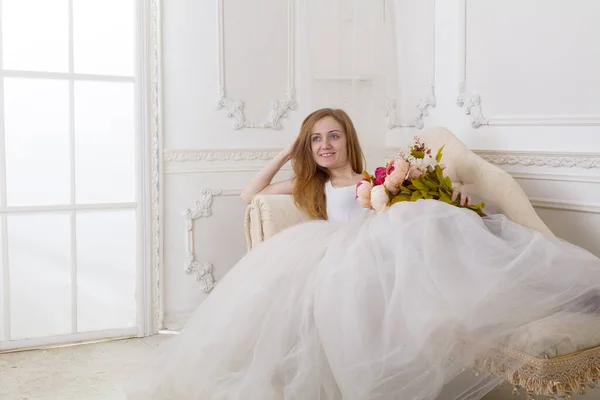 美しいです若い女性と花の服を着た白いフルスカートのドレスソファの上に座って — ストック写真