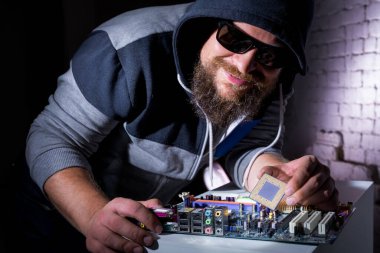 Güneş gözlüklü ve kapüşonlu bilgisayar korsanı donanımı kırıyor.