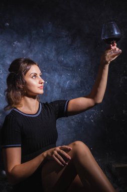 Siyah elbiseli güzel bir bayan bir bardak şarapla kürkün üzerinde oturuyor.