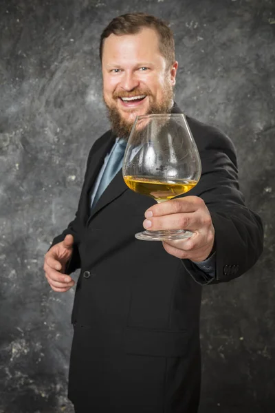 Solido uomo barbuto sorridente in giacca e cravatta con bicchiere di whisky — Foto Stock