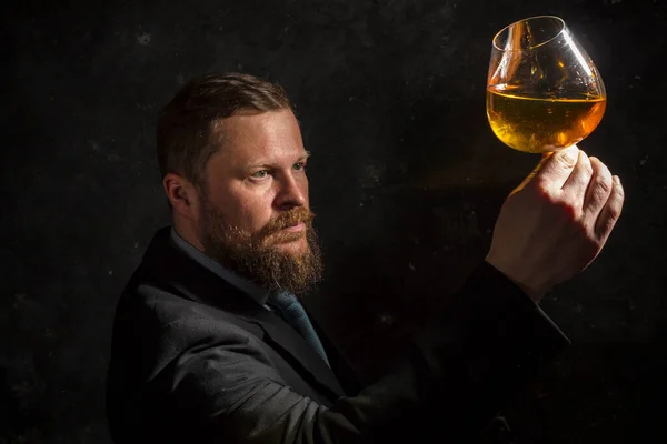 Hombre barbudo sólido y confiado en traje con vaso de whisky — Foto de Stock