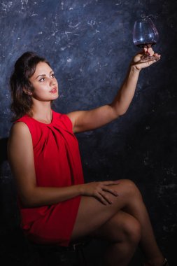 Kırmızı elbiseli güzel bir bayan bir kadeh şarapla oturuyor.