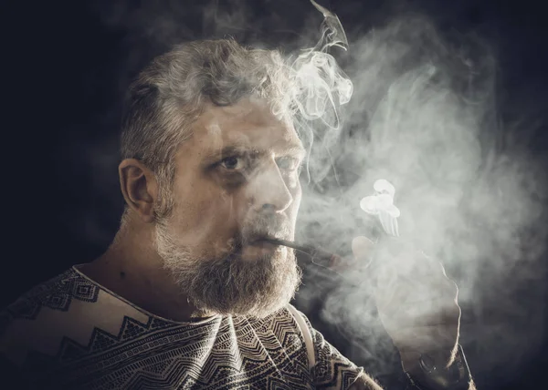 Твердый бородатый мужчина курит трубчатый портрет студии на черном фоне. — стоковое фото