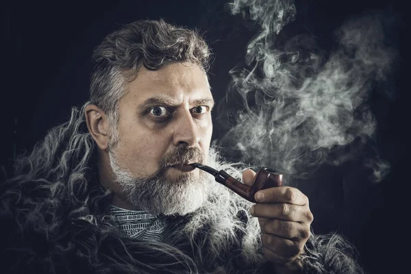 Hombre barbudo sólido en un manto de piel pipa humeante — Foto de Stock