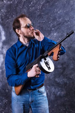 Makineli tüfekli, güneş gözlüklü, olgun bir adam.
