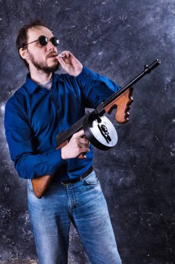Makineli tüfekli, güneş gözlüklü, olgun bir adam.
