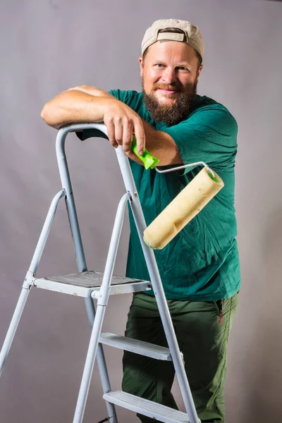 Fröhlicher bärtiger Polier im grünen T-Shirt mit Bürstenrolle und Leiter — Stockfoto
