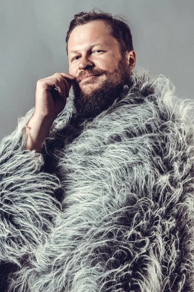 Solid bearded man in a fur mantle studio portrait