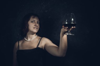 40 yaşında neşeli bir kadın, klasik giyinmiş, elinde şarap kadehi olan.