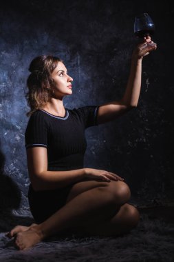 Siyah elbiseli güzel bir bayan bir bardak şarapla kürkün üzerinde oturuyor.